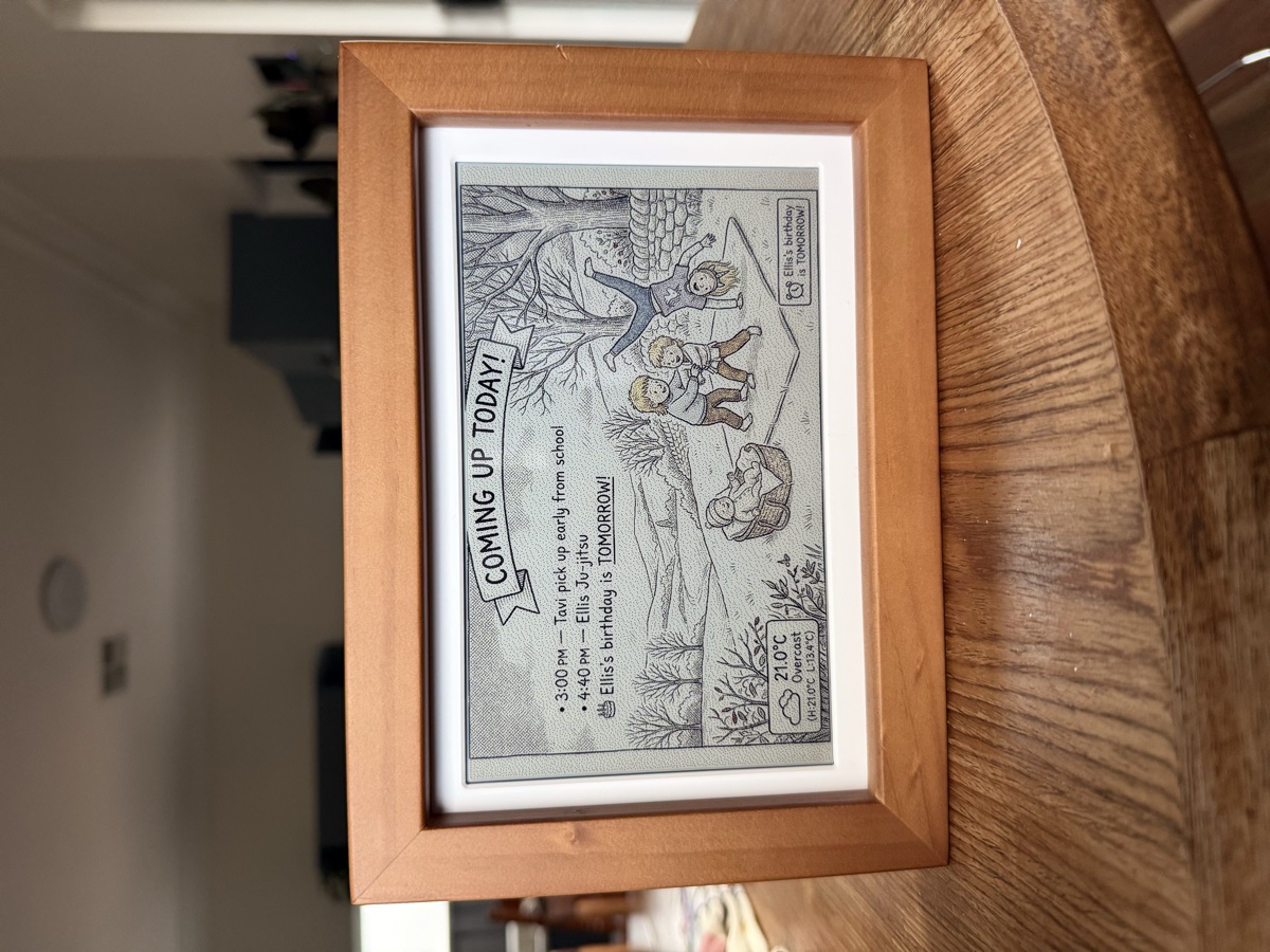 A Glanceboard e-ink display in a wooden frame, showing a hand-drawn illustration of kids playing with their day's schedule